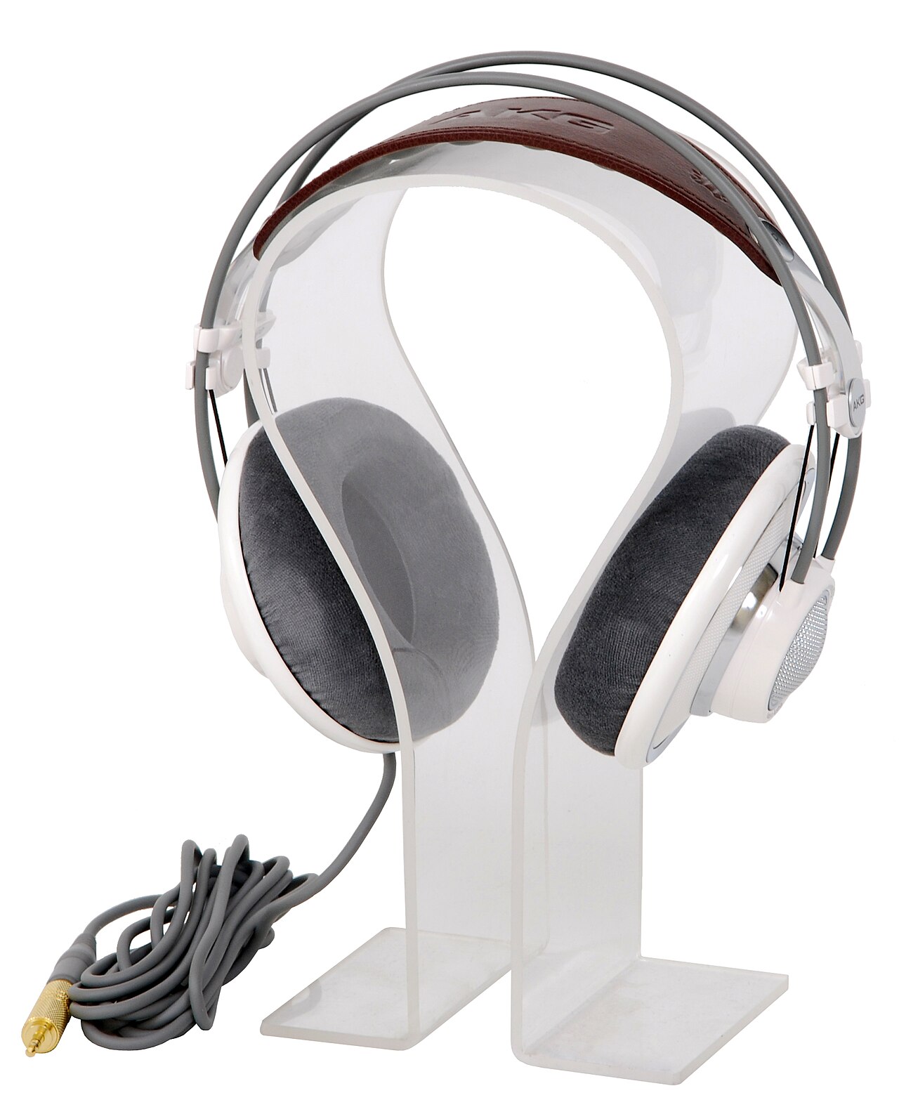 Over-ear reference headphones with large cushioned ear pads and a suspended leather headband are displayed on a transparent acrylic stand, with a coiled gray audio cable and a gold-plated connector placed neatly in front